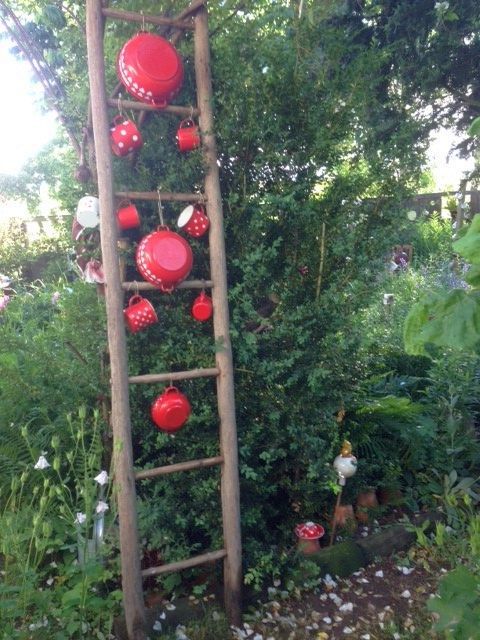 A wooden ladder in the garden, hung with red pots and cups with white dots.