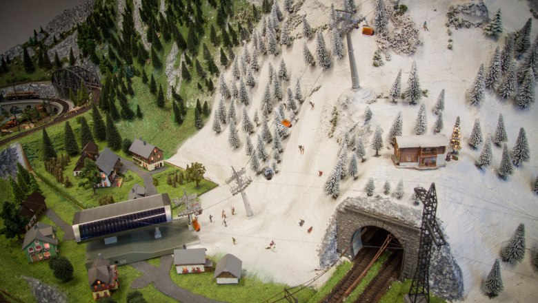 Model landscape with mountains, skiers, cable car and railroad tunnel.