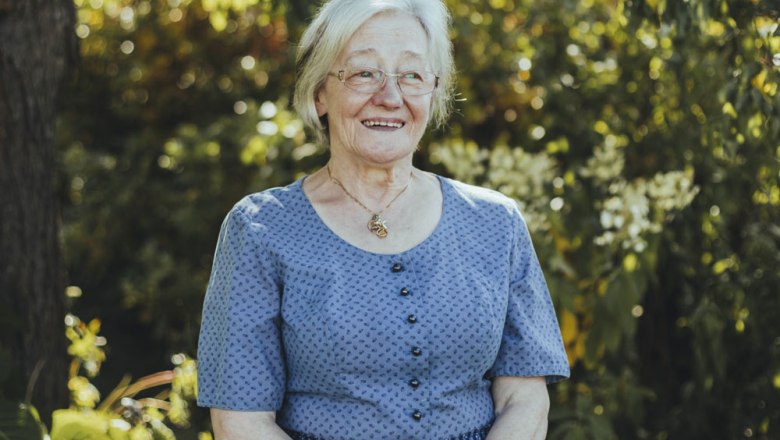 Older woman in blue clothes smiling outdoors.