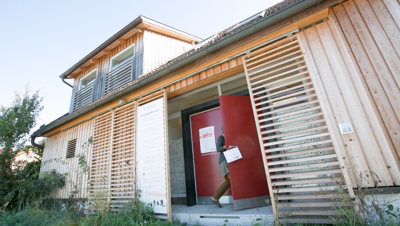 A modern wooden building with a red door and a person entering the building.