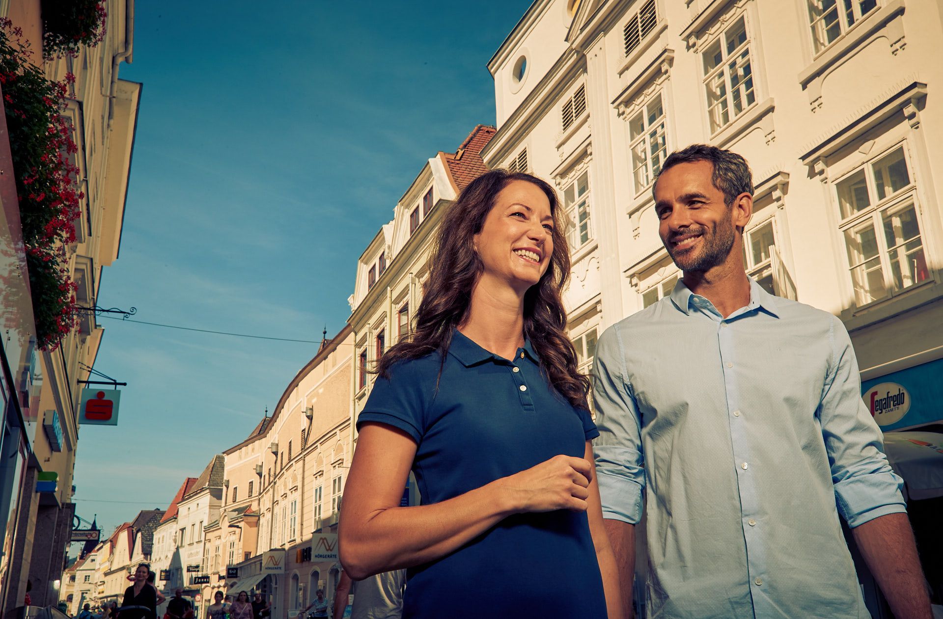 A smiling couple strolls through the old town of Krems in sunny weather.