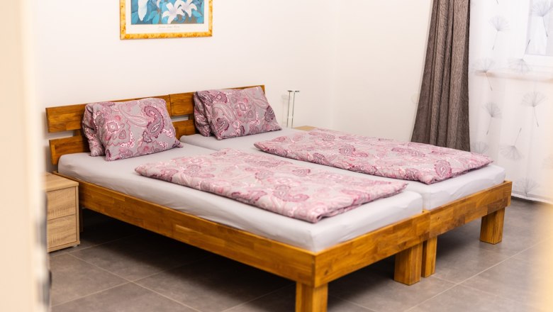 A bedroom with two single beds standing together and pink patterned comforters. A picture with a floral motif hangs on the wall.