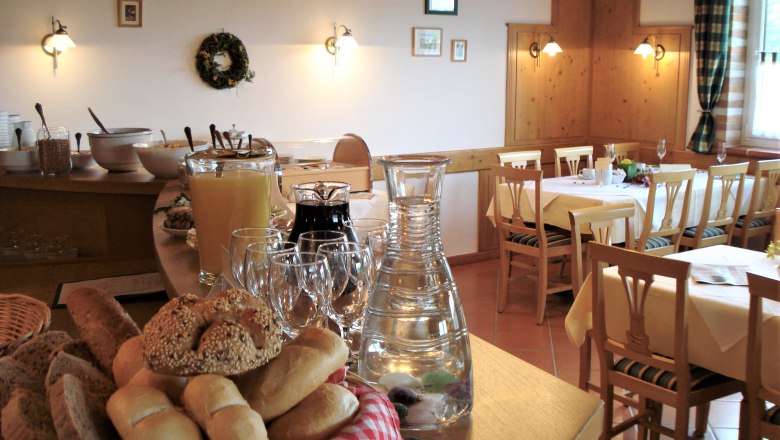 A breakfast room with laid tables, bread basket, juice and water jug on a buffet.