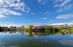 Exterior view of the cheese maker's world with blue sky and lake in the foreground.