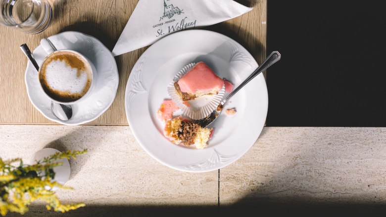 A plate with half a punch doughnut and a cup of coffee on a table.