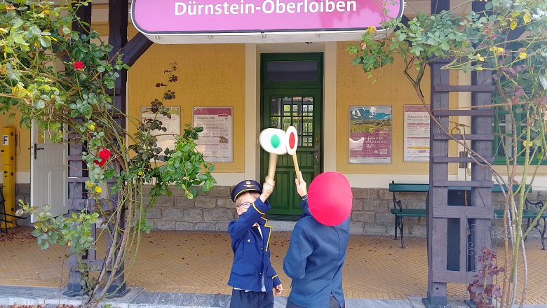 Adventure vacation for railroad enthusiasts, © Bernhard Kaar Two children in railroad uniforms stand in front of Dürnstein-Oberloiben station holding up signal boards.