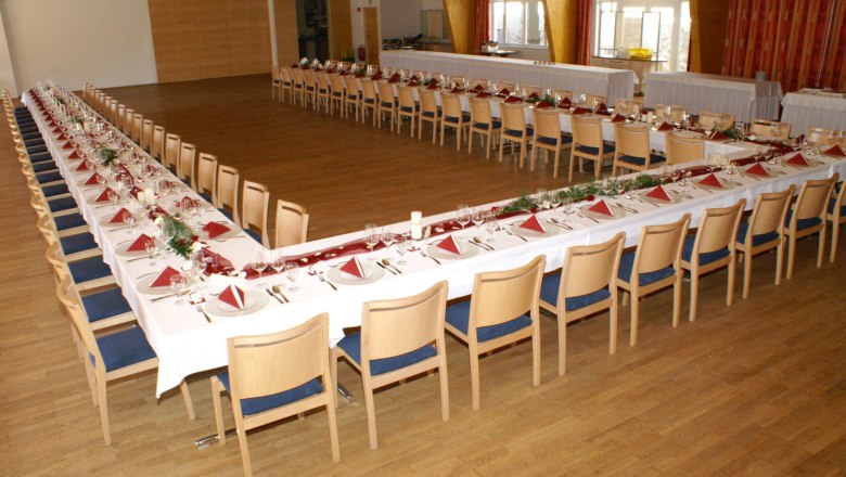A large ballroom with tables set in a U-shape, decorated with red napkins and flowers.