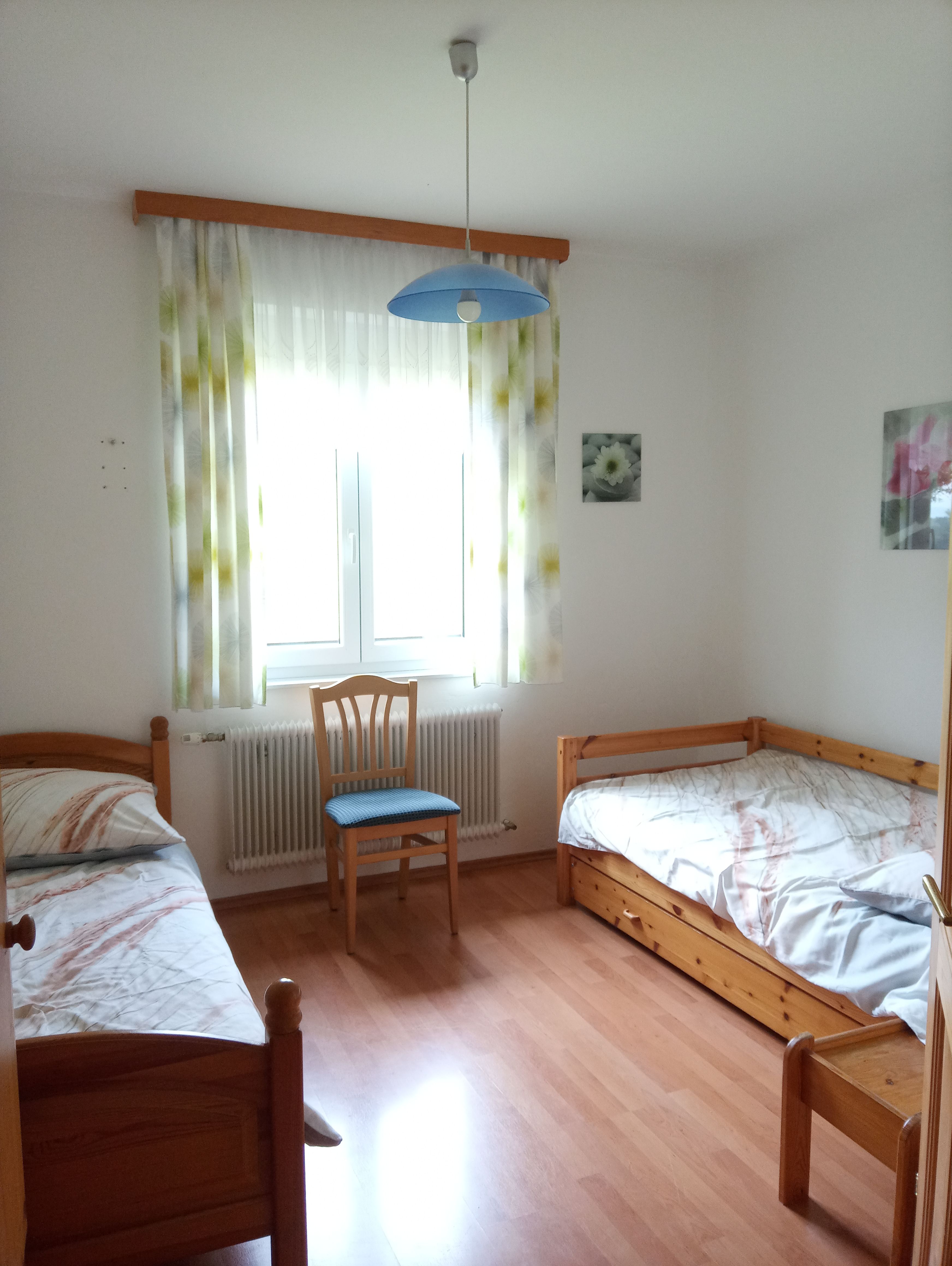 A simply furnished bedroom with two single beds, a chair and a window with curtains.