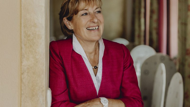 Woman in a red blazer smiles and leans against a wall.