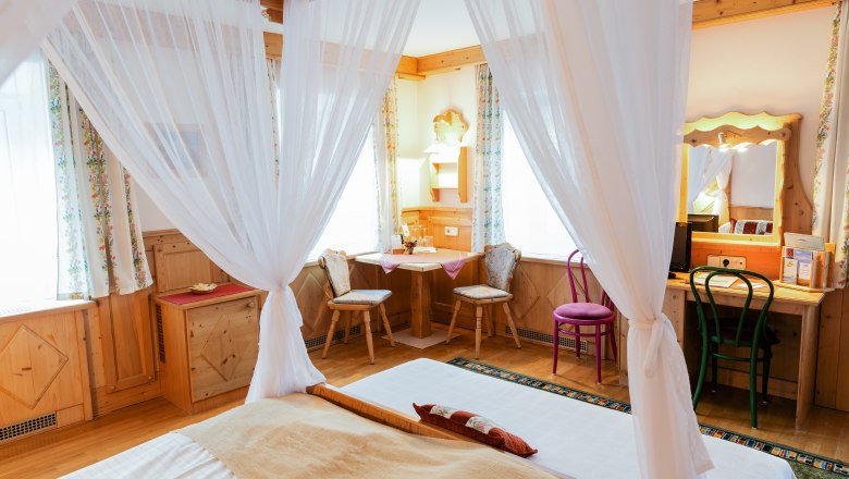 Cozy double room with four-poster bed, wooden furniture and desk.
