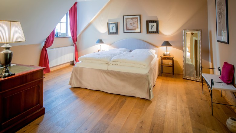 A cozy double room with wooden floor, a large bed, red curtains and stylish decorations.