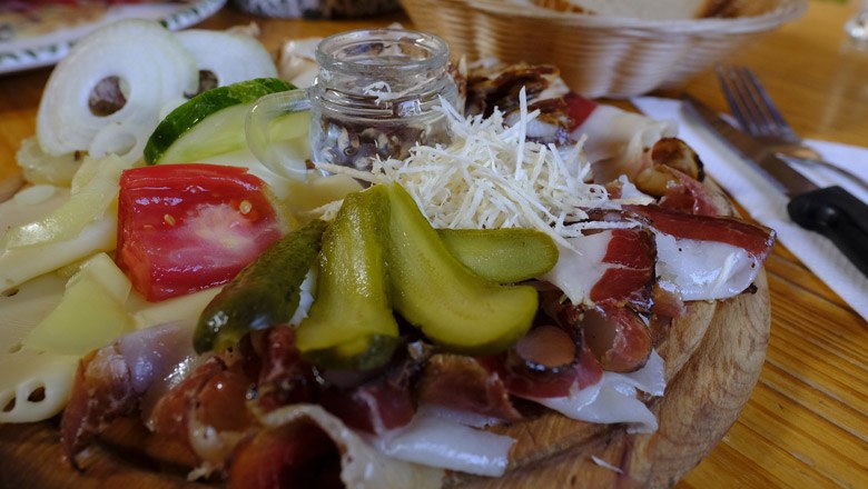 A rustic platter with sausage, cheese, gherkins and tomatoes on a wooden table.