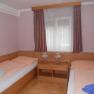 A simply furnished room with two single beds, a window with curtains and a small table with two lamps.
