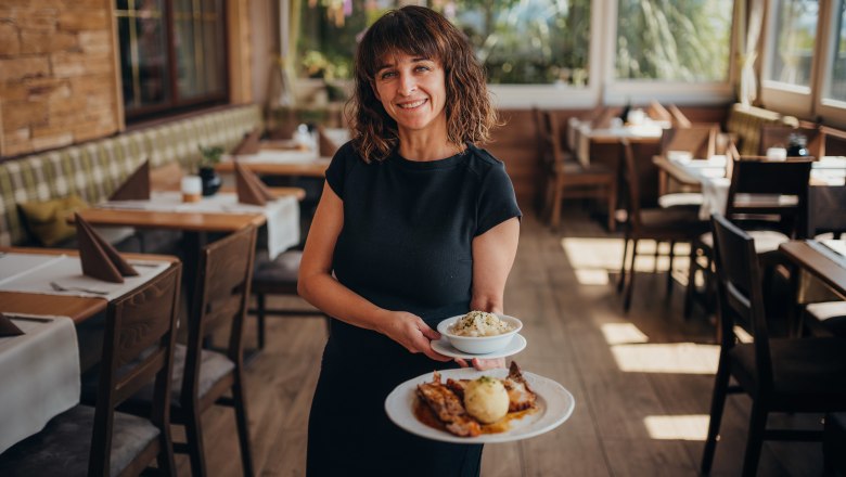 Woman serves food in a cozy restaurant with wooden furniture.