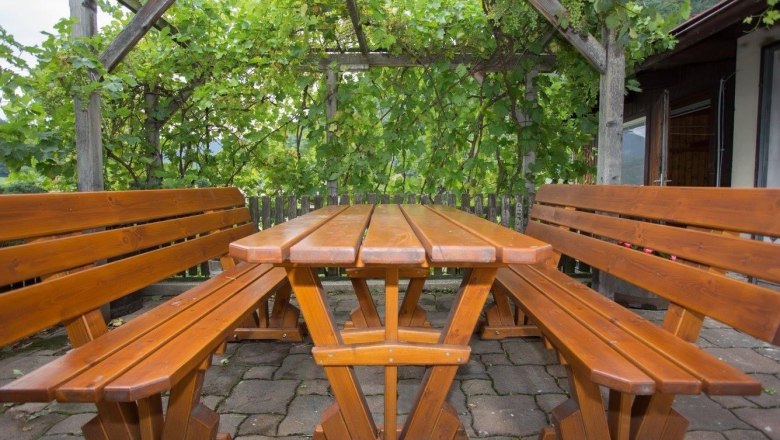Wooden table and benches outside under a pergola with vines.