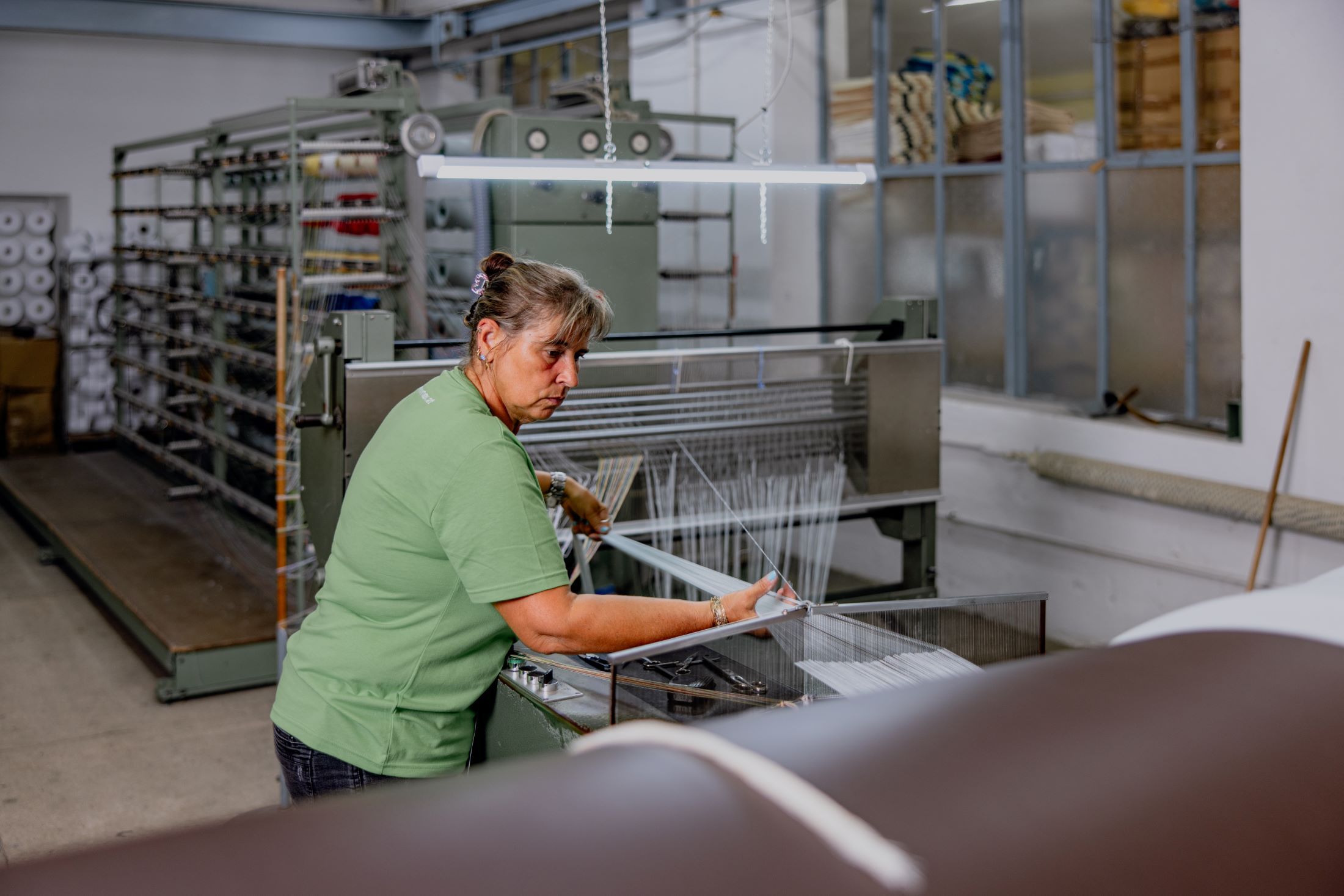 Woman working on a weaving machine in a textile factory.