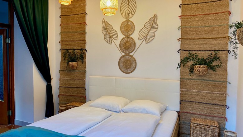 A cozy bedroom with a double bed, decorative tapestries and plants.