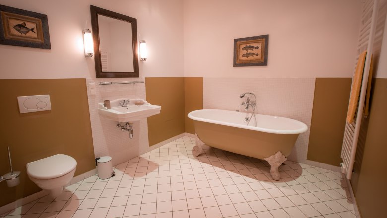 Elegant bathroom with free-standing bathtub, washbasin, mirror and WC. Walls in beige and white, decorated with fish pictures.