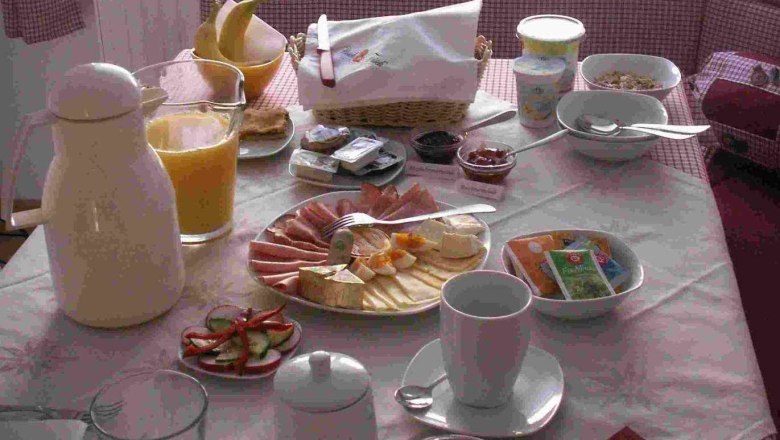 A laid breakfast table with bread rolls, cold cuts, cheese, juice and crockery.