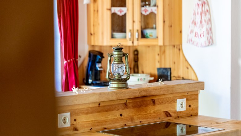 Wooden kitchen sideboard with ceramic hob, lantern on the counter, box and red curtain in the background.