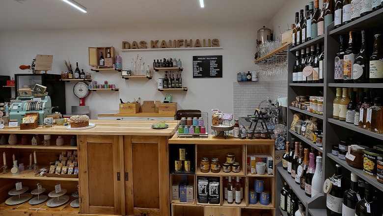 Interior view of a small, cozy store with wooden shelves filled with bottles of wine, groceries and an old cash register.