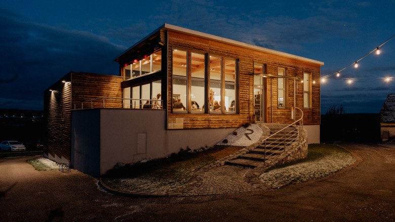 Exterior view of a modern wine tavern at night with illuminated windows and fairy lights.