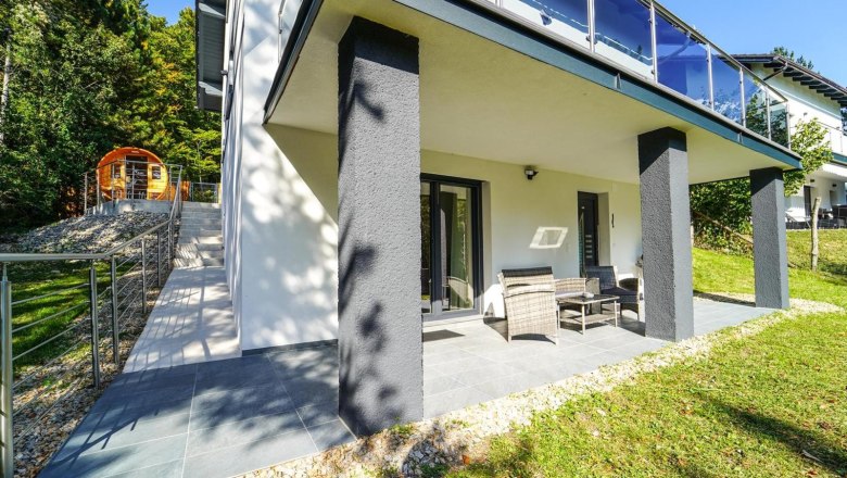 Terrace of a modern vacation home with garden furniture and adjoining garden.