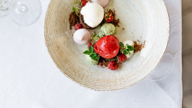 A dessert with various scoops of ice cream, raspberries and mint leaves on a plate.